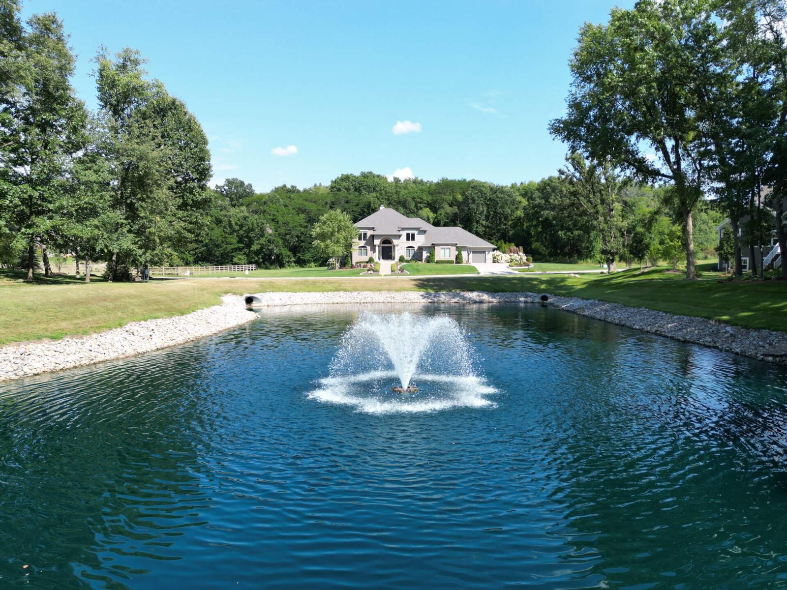 Pond with fountain and a home beyond the lawn